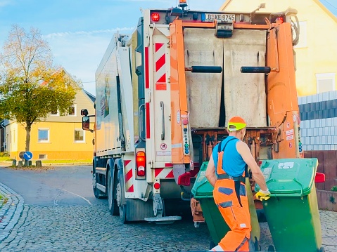 Ingersheim, Germany - October, 17 - 2022: Garbage worker pushes two garbage cans to the truck.