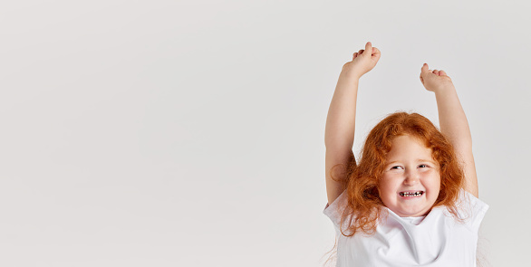 Happiness. Thrilled little girl, kid shouting in rejoice and raising hands up isolated over white background. Concept of children positive emotions. Copy space for ad