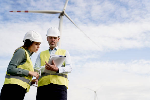 istock Two caucasian engineers standing on wind turbine field and discussing over documents 1434714000