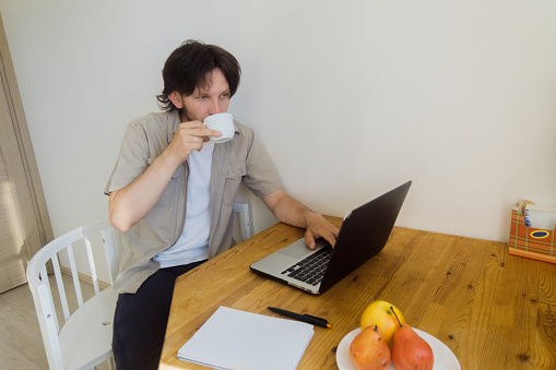 bearded young man drinks coffee without looking up from work. Remote work concept. Copy space.