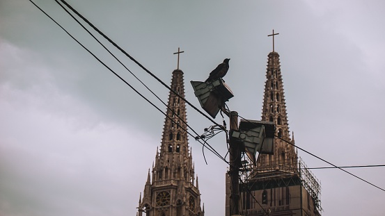 A low-angle of the cathedral of Zagreb with power lines and gloomy, cloudy background