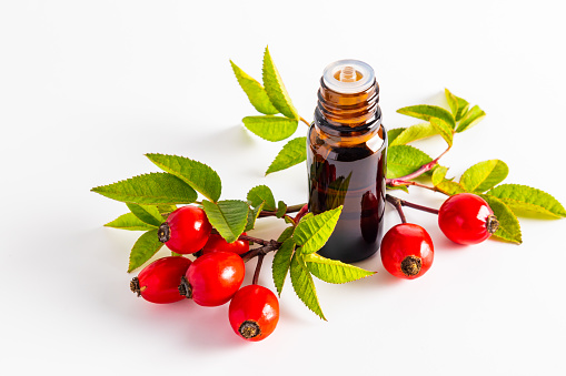 a medical bottle with a dark glass dropper with organic rosehip seed oil on a white background among ripe berries. Mock-up