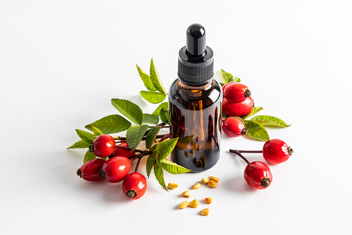 serum based on rosehip seed oil for facial skin care in a cosmetic bottle on a white background among ripe rosehip berries. moistening. nutrition