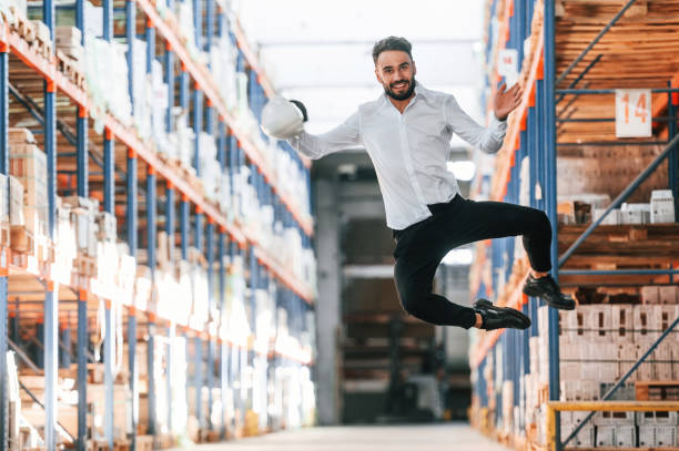 istock Jumping, having fun. Storage worker is in the warehouse with bunch of products 1434723748
