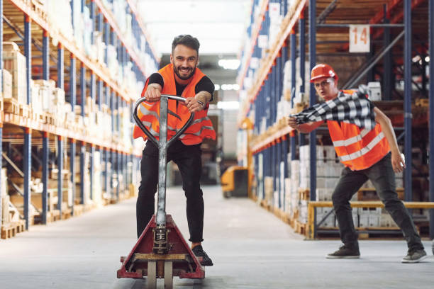 istock Man riding trolley platform. Having fun. Two storage workers is in the warehouse 1434723963