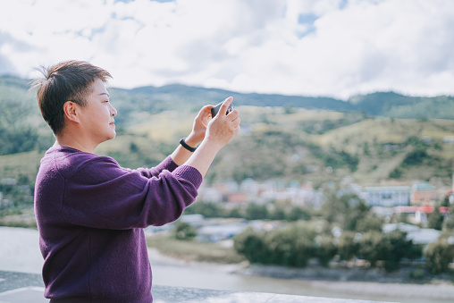 Asian Chinese female solo traveller photographing in front of Punakha , Bhutan with smart phone