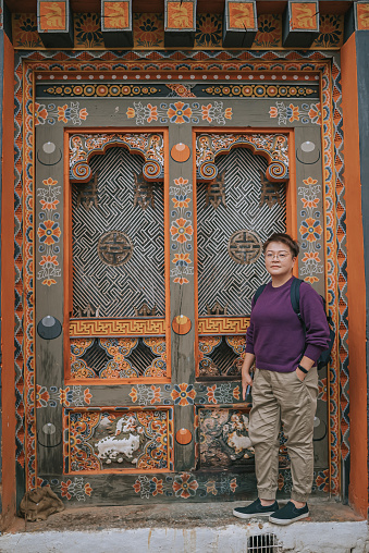 Asian Chinese female solo traveller standing in front of Punakha Dzong looking at camera smiling