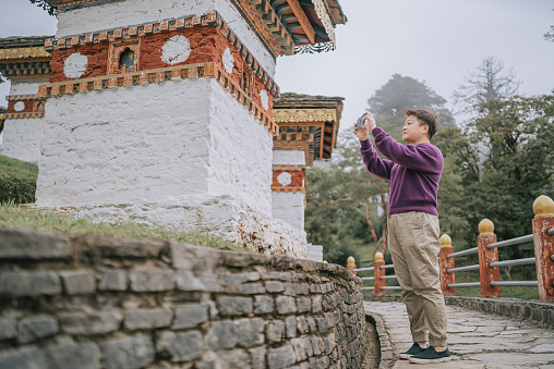 Asian Chinese female solo traveller photographing in front of Dochula Pass , Bhutan with smart phone