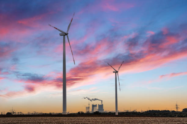 Looking at two huge wind power turbines in front a of a coal powered energy plant.