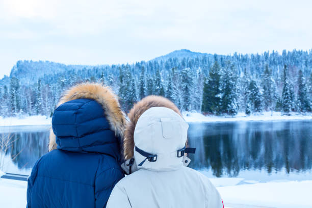 chicas excursionistas con chaquetas de plumas de pie cerca del río contra el bosque de invierno. concepto de viaje. - siberia river nature photograph fotografías e imágenes de stock