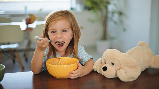 Adorable little girl sitting at kitchen table eating a bowl of cereal