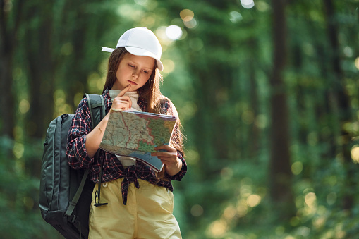 Using the map. Girl is in the forest at summer day time discovering new places.