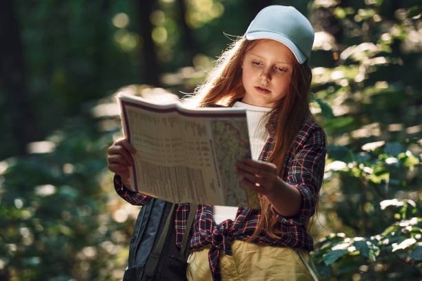 Holding map in hands. Girl is in the forest at summer day time discovering new places.