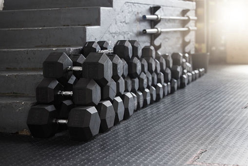 Closeup of a group of gym weights on the floor in an empty health and sports club. Macro view of dumbbells barbell weights in a dark exercise room. Get to the gym to increase your health and fitness