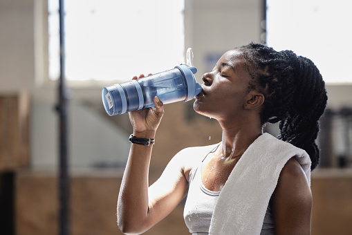 Drinking water and relax after a fitness, workout and exercise training of a woman athlete. Female from Nigeria with sweat done reaching target cardio sports goal at a health, wellness and sports gym
