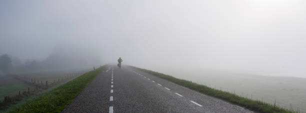 człowiek na rowerze przejażdżki we mgle na grobli w pobliżu renu w holandii - lag zdjęcia i obrazy z banku zdjęć