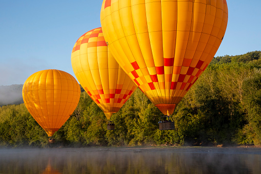 yellow and red hot air balloons fly low over dordogne river under blue sky in southern france