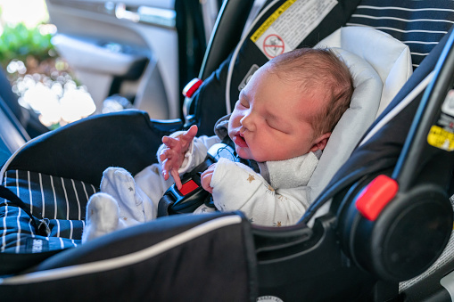 A cute multiracial newborn baby sleeps while strapped in an infant carseat. The 2 day old baby was just discharged from the hospital and is on his way home.
