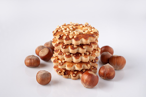 a stack of shortbread cookies with nuts and scattered hazelnuts on a white glass