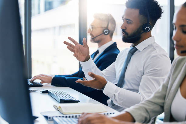 centro de llamadas, atención al cliente y soporte con un consultor en un auricular que trabaja en una computadora en su oficina. contáctenos, crm y telemarketing con un consultor masculino en una llamada en su escritorio de trabajo - centro de llamadas fotografías e imágenes de stock