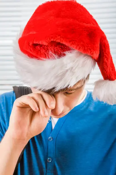 Sad Young Man in Santa Hat weeps on the Jalousie Background
