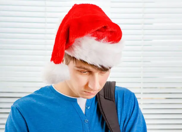 Sad Young Man in Santa Hat on the Jalousie Background