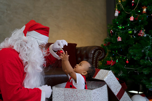 Santa Claus and a little boy. Boy tells wishes in front of Christmas Tree