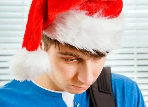 Sad Young Man in Santa Hat on the Jalousie Background closeup