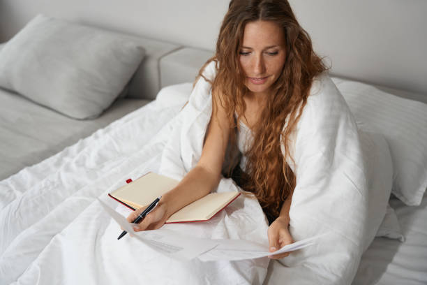 istock Woman taking notes in notebook in bed covered with blanket 1434739248