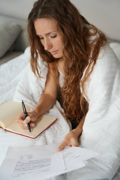istock Woman copying information from a printout into notebook in bed 1434739254
