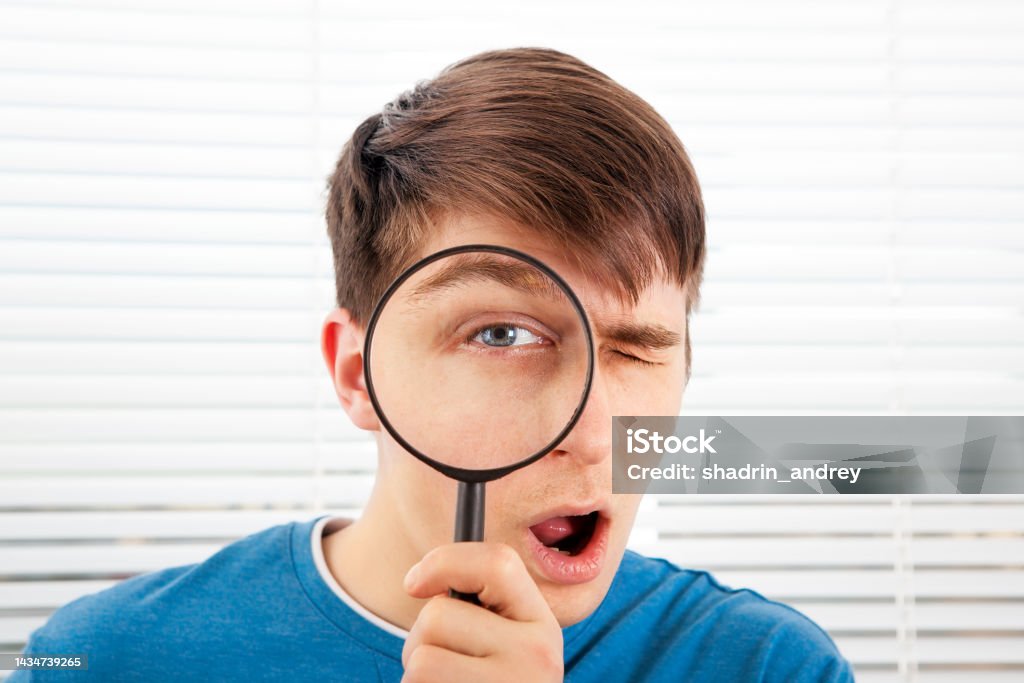 Young Man with a Magnifying-glass Young Man with a Magnifying Glass on the Jalousie Background closeup 25-29 Years Stock Photo