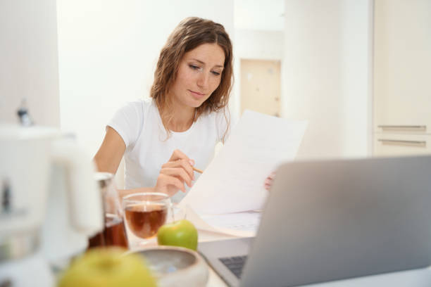 istock Woman reading and checking text on paper at table in kitchen 1434739288