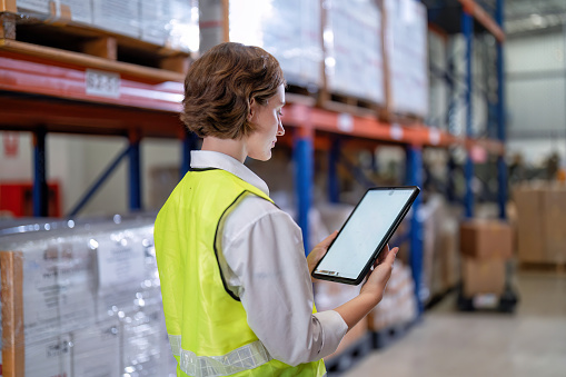Worker in warehouse hold tablet check list perform inventory stock check goods boxes on the storage steel racking for annual report