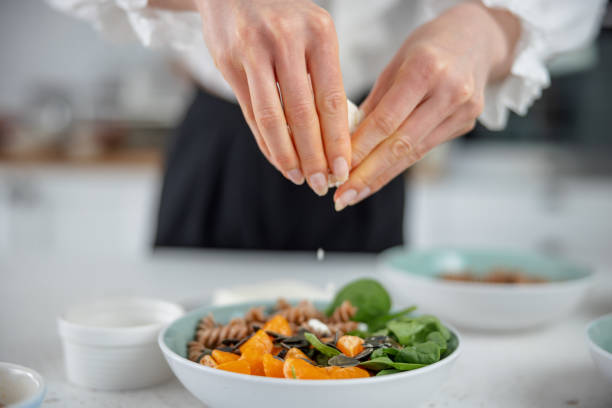 Closeup Of The Hands Of A Young Caucasian Woman Adding Grated Cheese Over A Salad stock photo