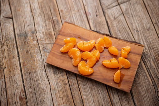 Aerial view of chopped juicy tangerine slices over a wooden chopping board placed over a wooden table with pronounced cracks.