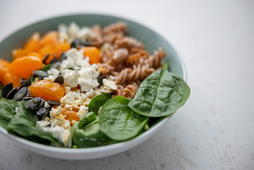 Closeup of a colorful and delicious healthy salad making focus on the spinach, cheese, pumpkin seeds and tangerines. The background is defocused and the colors of the salad are very bright. The salad plate is placed over a white surface.