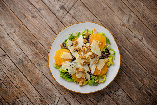 Aerial view of A healthy colorful salad with lettuce, orange slices, black beans, cheese, walnuts And dressing on a white ceramic plate placed over an old wooden table.