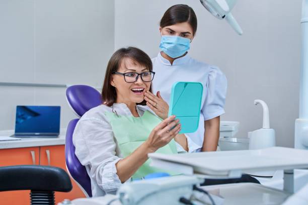 Woman patient together with dentist, patient sitting in dental chair looking at mirror stock photo