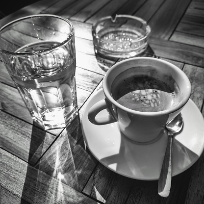 Vertical high angle closeup black and white photo of a cup of latte coffee on a wooden table in a cafe. Soft focus cafe background.