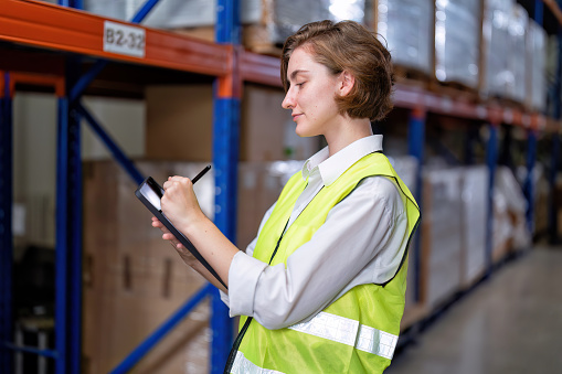 Worker in warehouse hold tablet check list perform inventory stock check goods boxes on the storage steel racking for annual report