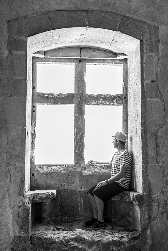 Male tourist resting on a window bench of an ancient castle. Black and white photo.