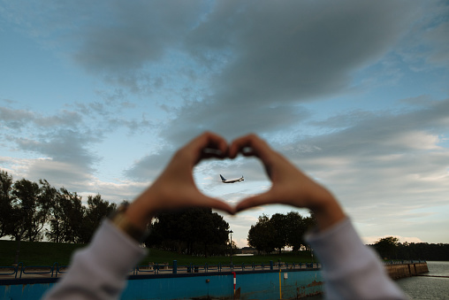 Hands making a heart shape with an airplane taking off inside
