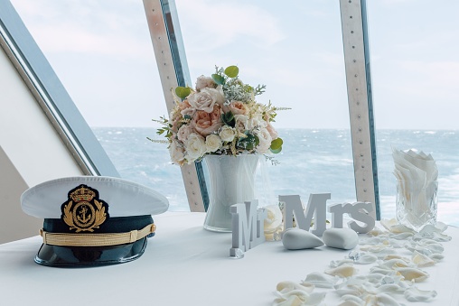 A beautiful wedding table decorated with a sailor hat and flowers with the sea behind the window