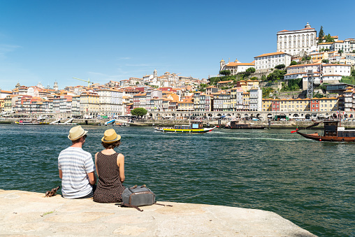 Man and woman couple resting at Douro River quay while are looking at Porto views and Rabelo boats. Sightseeing in Portugal.