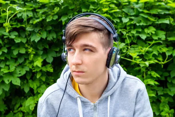 Sad Young Man in Headphones on the Green Leaves Background outdoor