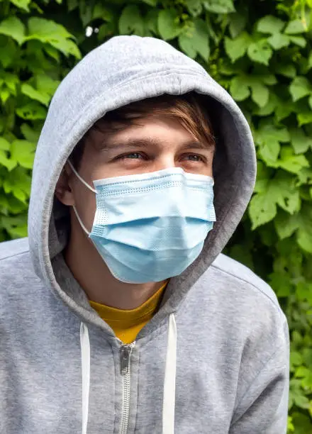 Young Man in the Surgical Mask on the Green Leaves Background