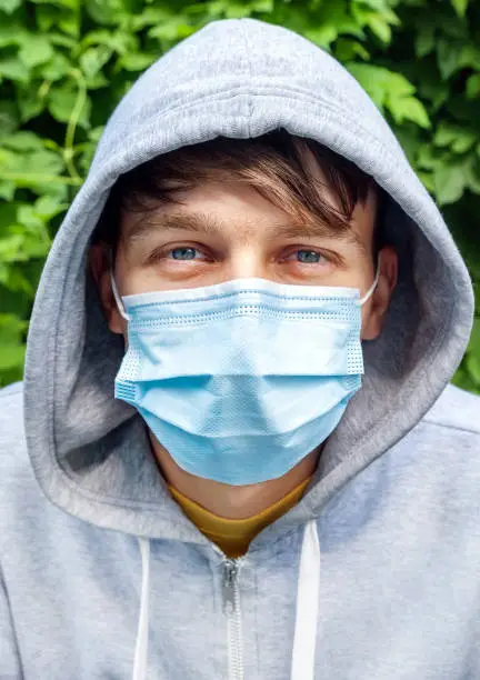 Young Man in the Surgical Mask on the Green Leaves Background