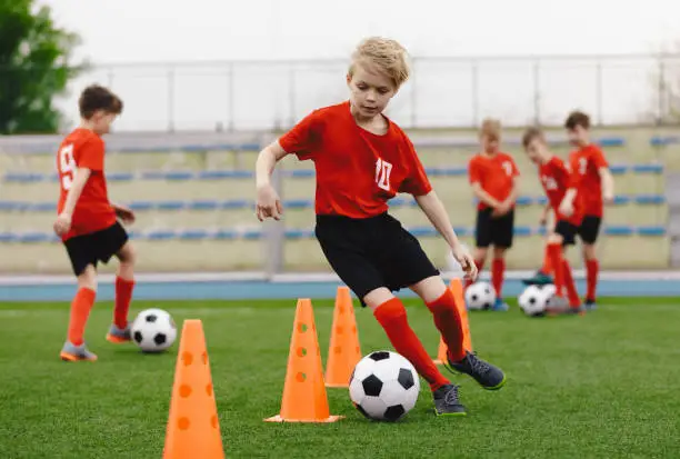 Boys on soccer football training. Young players dribble ball between training cones. Soccer summer training camp. Players on football practice session