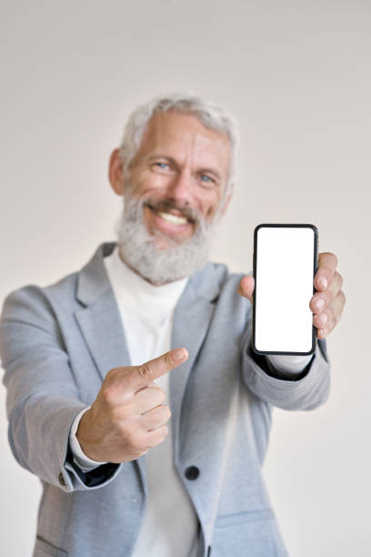 istock Old business man pointing at phone with white mock up screen, vertical. 1434763181