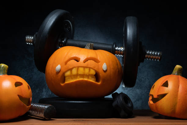 istock Halloween gym concept with carved pumpkin lifting dumbbells. 1434763517